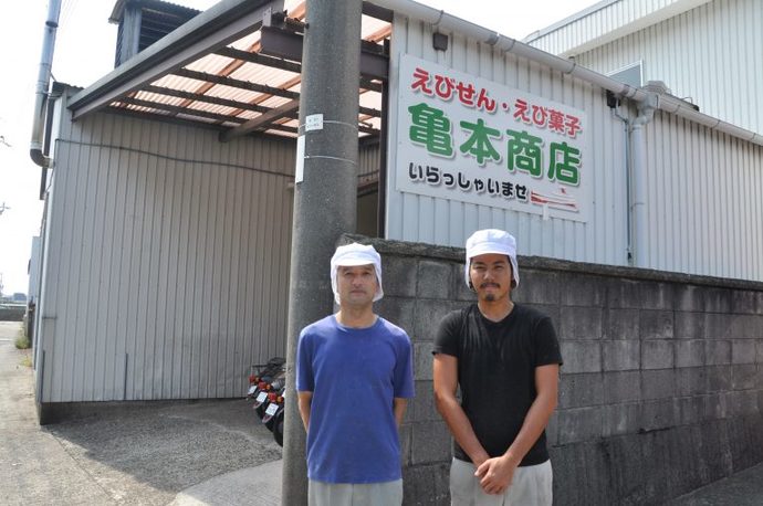 工場の前にて、白い工場用帽子をかぶって立つ、男性従業員2人の写真