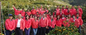 みかん畑にて、赤い制服を着た、笑顔の従業員全員集合の写真