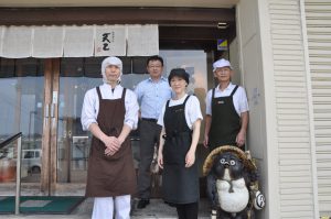 お店の前に立つ、ワイシャツ姿の男性1人と調理用の白い帽子とエプロンをつけた男性従業員2人と、黒いエプロンをつけた女性従業員1人の写真