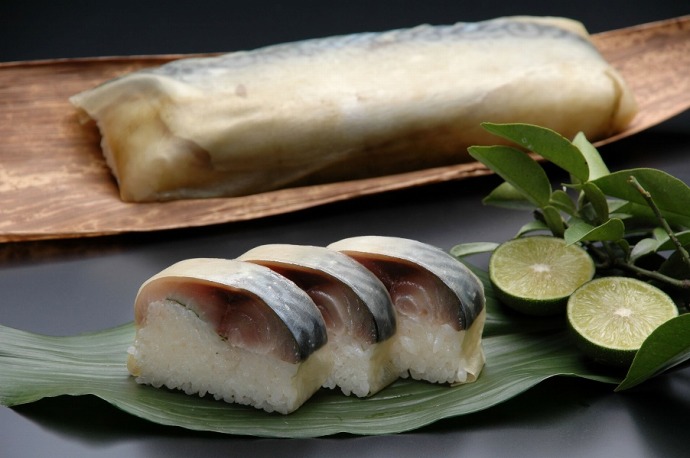 竹皮に乗るさば寿司と、笹の葉にゆずとともに並べられた一口大のさば寿司の写真
